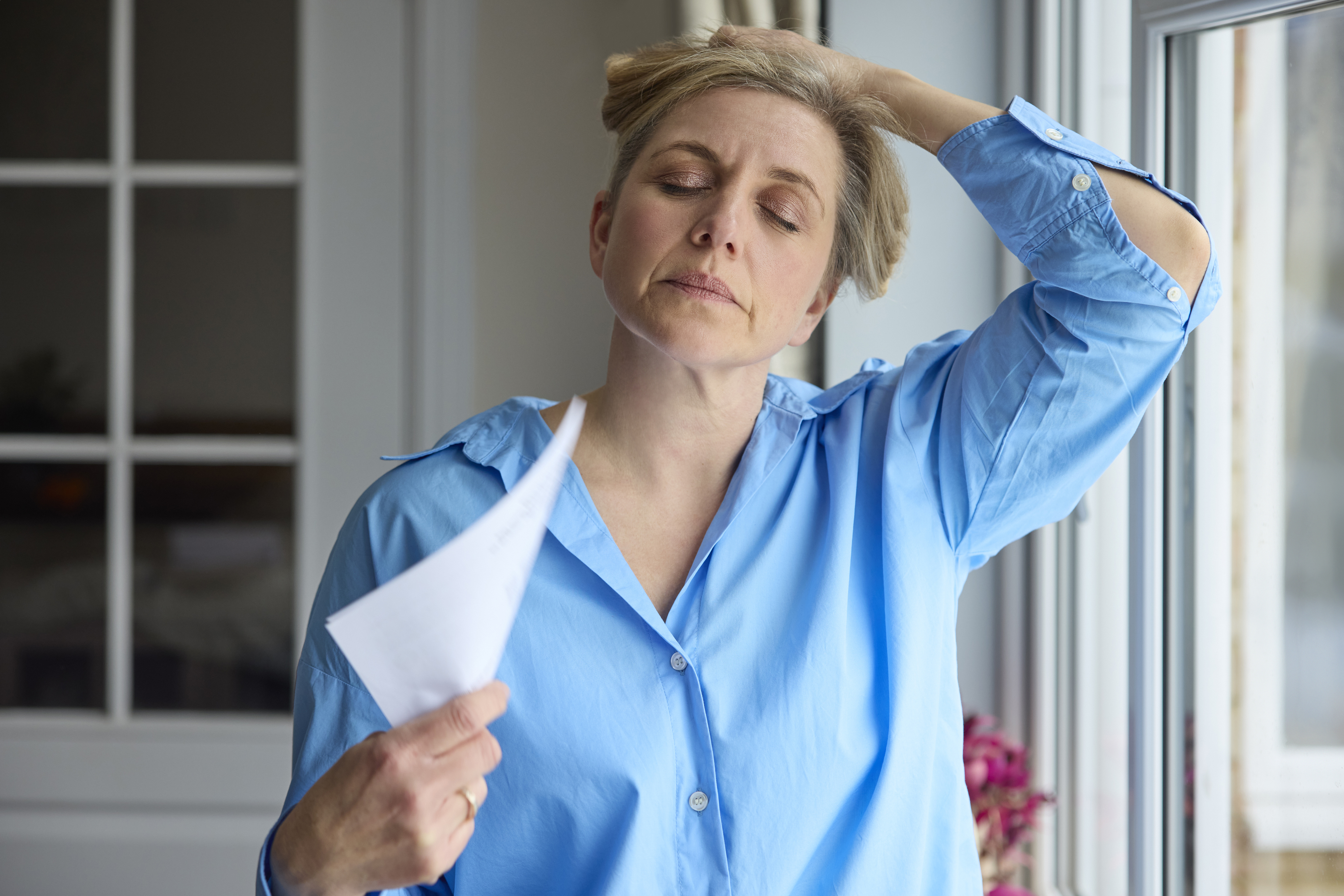 woman standing near window fanning herself