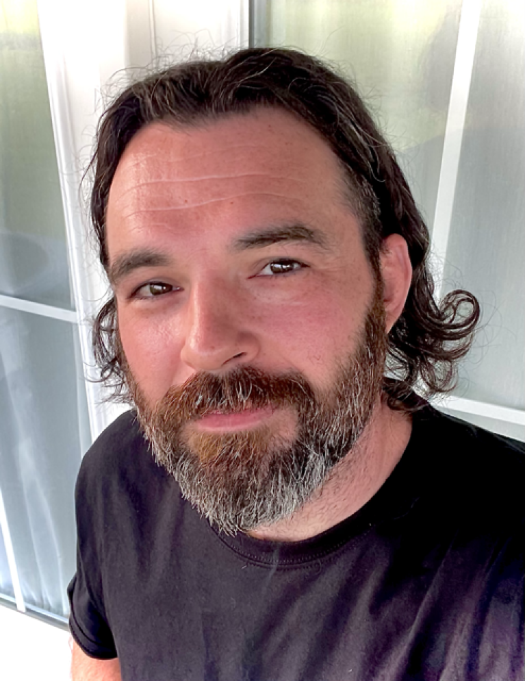 A man with shoulder length hair and a beard looking up at the camera