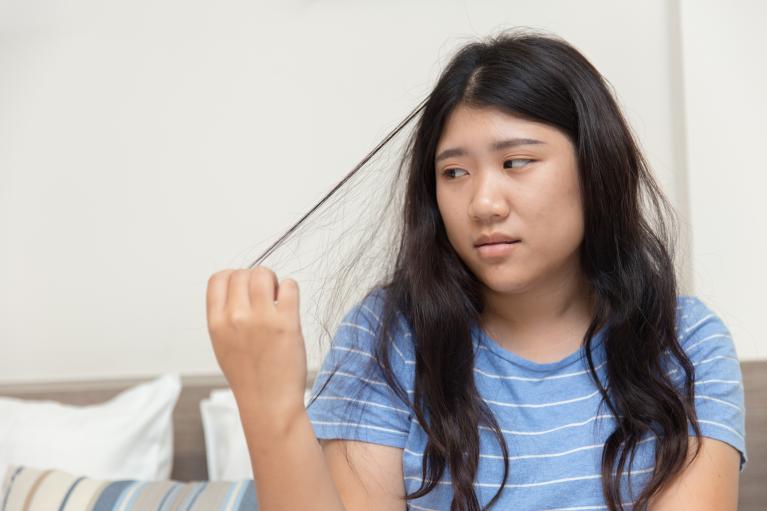 Teen girl in blue shirt pulling at a piece of her long black hair 