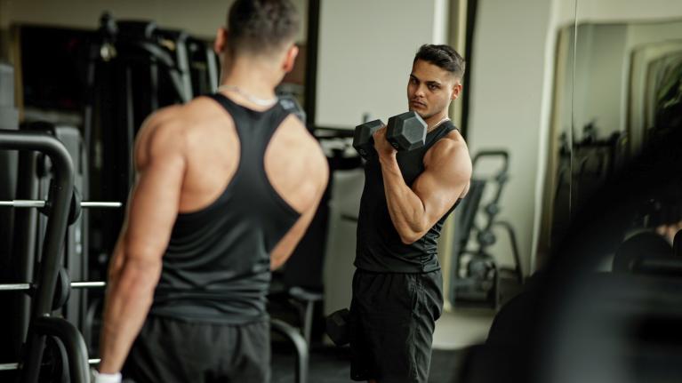 man wearing black tank top lifting dumbbells in front of mirror