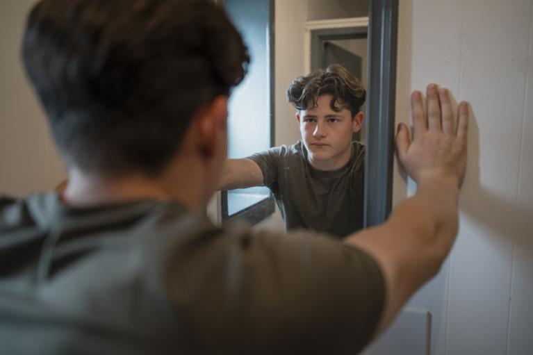 Teenage boy looking into the mirror at his reflection and not happy with what he sees
