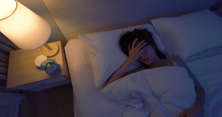 woman laying in bed with a lamp on and struggling to sleep