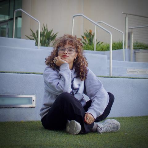 girl siting on the grass with her legs criss-crossed wearing jeans and a hoodie.