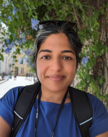 Woman standing outside wearing a blue shirt, black backpack and sunglasses on her head