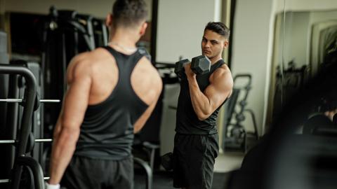 man wearing black tank top lifting dumbbells in front of mirror