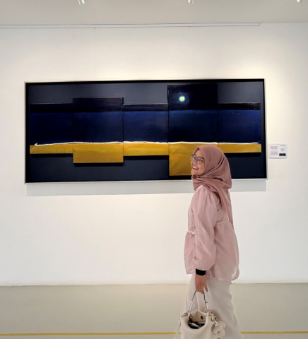 Devia Fitaloka walking in an art museum wearing a pink blouse and white pants holding a purse