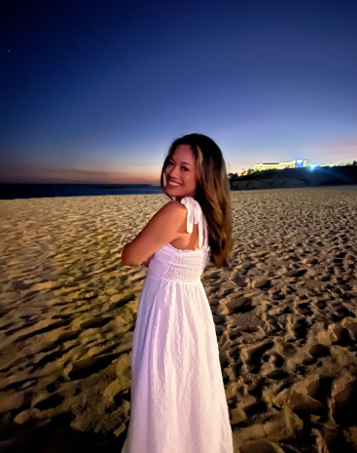 woman wearing a white dress standing on a beach at sunset