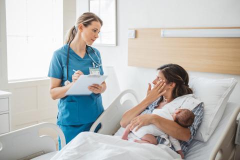 woman sitting in hospital bed with baby after just having given birth, nurse with clipboard standing next to bed