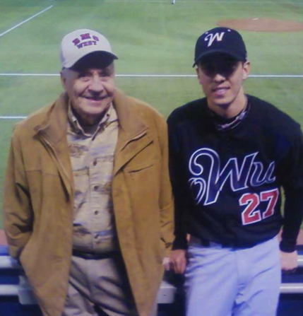 An older man standing next to a young man in a baseball uniform at a baseball field
