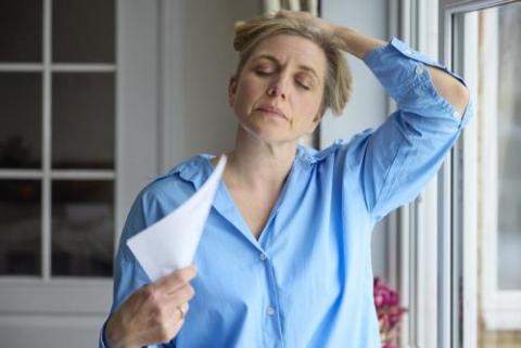 woman standing near window fanning herself