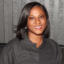 Professional headshot of a woman with short, dark hair wearing a black top, smiling warmly at the camera.